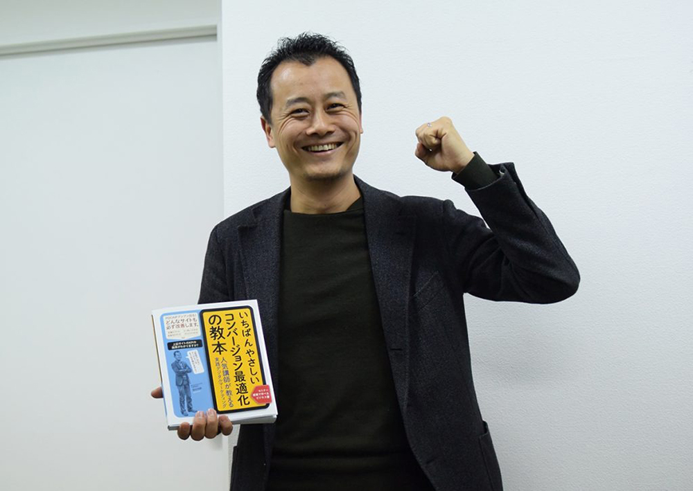 写真：著作「いちばんやさしいコンバージョン最適化の教本」をもってがっつぼをする弊社代表・深田