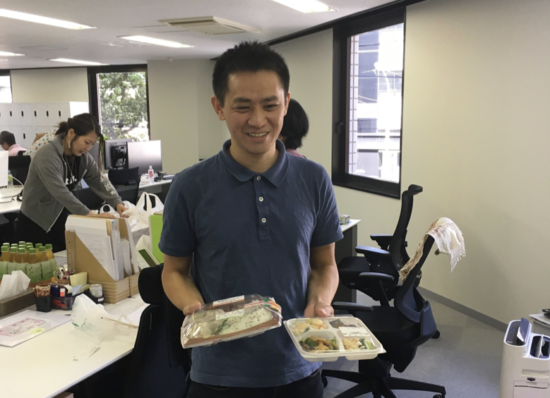 写真：優勝した茂木さん。ミニストップのシュウマイ弁当を持って苦笑い