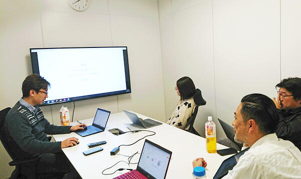 写真：社内勉強会の様子。会議室に集まったメンバーとオンライン参加のメンバー。