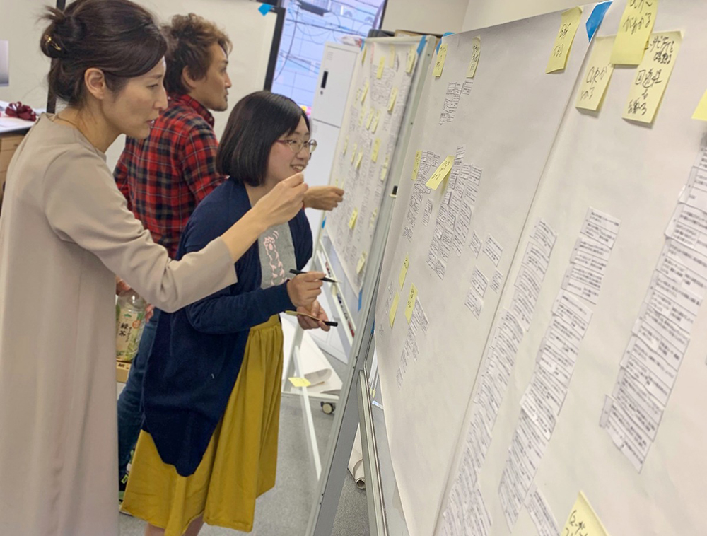 写真：社内ワークショップの様子。付箋に書かれた価値マップを、みなで検討中。
